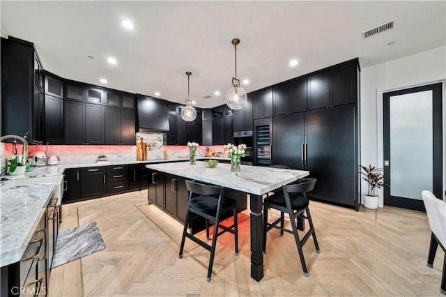 kitchen featuring visible vents, a sink, light stone counters, decorative backsplash, and dark cabinets