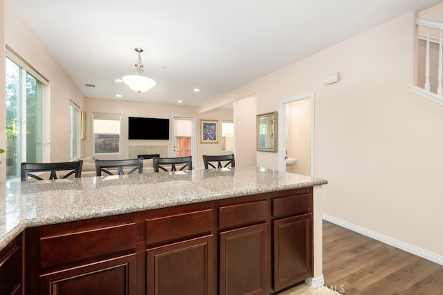 kitchen with hanging light fixtures, a breakfast bar, light hardwood / wood-style flooring, and light stone counters