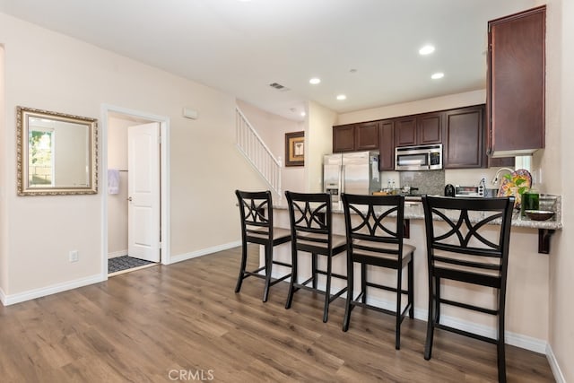 kitchen featuring dark wood-type flooring, appliances with stainless steel finishes, a kitchen bar, and tasteful backsplash