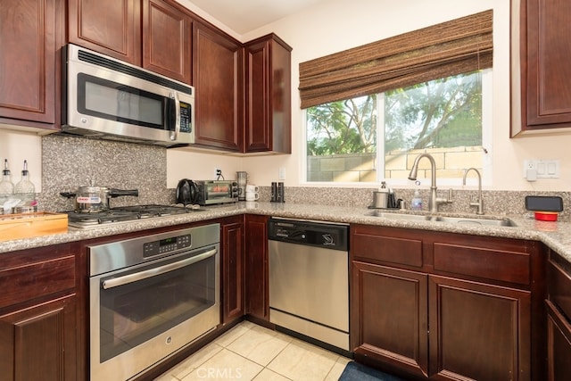 kitchen with backsplash, sink, light stone countertops, light tile patterned floors, and appliances with stainless steel finishes