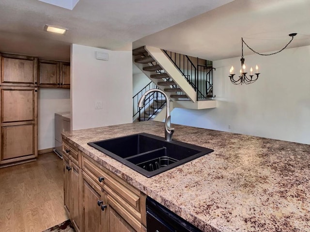 kitchen with hanging light fixtures, independent washer and dryer, sink, an inviting chandelier, and light hardwood / wood-style floors