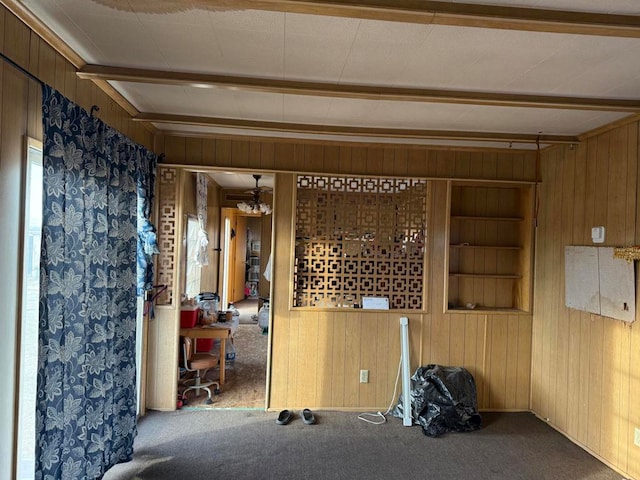 carpeted spare room with beam ceiling, wooden walls, and built in shelves