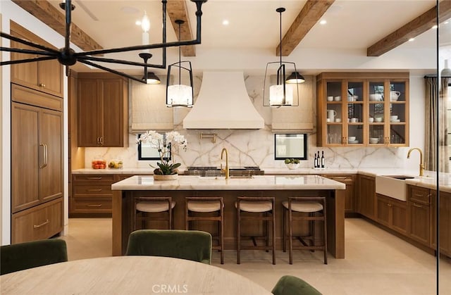 kitchen featuring custom exhaust hood, a kitchen island with sink, a kitchen breakfast bar, tasteful backsplash, and beam ceiling