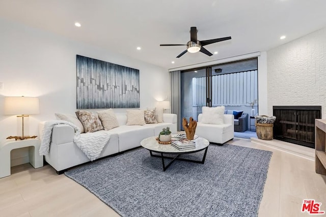 living room featuring ceiling fan, a large fireplace, and light hardwood / wood-style floors