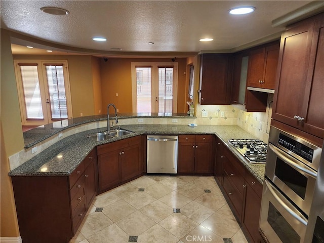 kitchen with appliances with stainless steel finishes, french doors, dark stone counters, sink, and kitchen peninsula