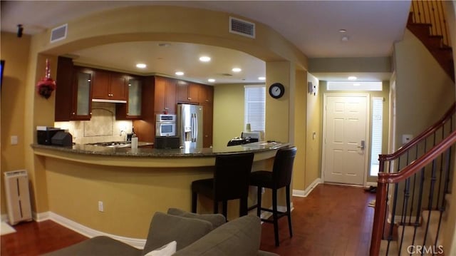 kitchen featuring radiator heating unit, stainless steel appliances, dark stone counters, backsplash, and dark hardwood / wood-style floors