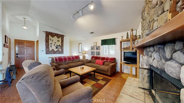 living room with a fireplace, track lighting, light hardwood / wood-style floors, and lofted ceiling