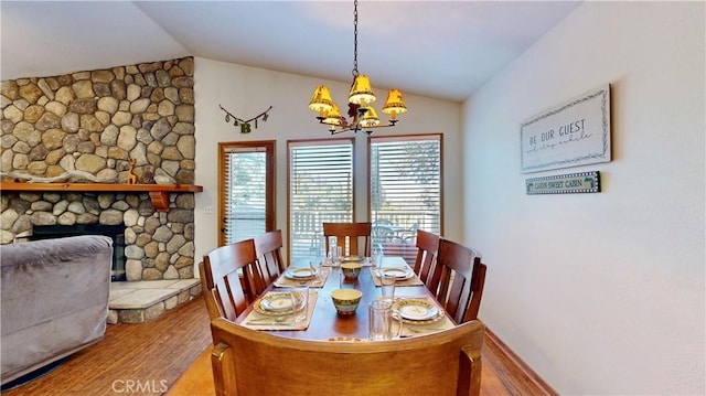 dining area featuring a chandelier, hardwood / wood-style floors, vaulted ceiling, and a stone fireplace