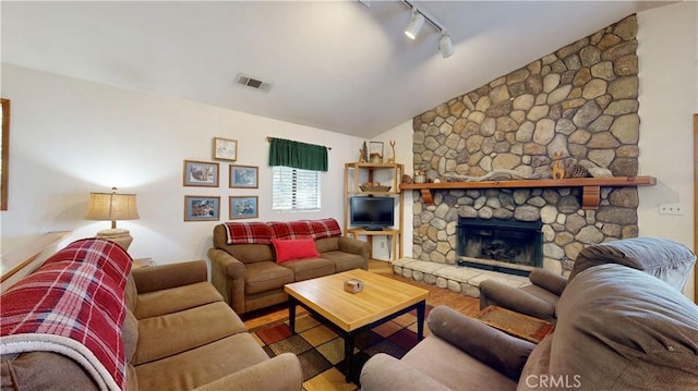 living room with hardwood / wood-style floors, rail lighting, vaulted ceiling, and a stone fireplace