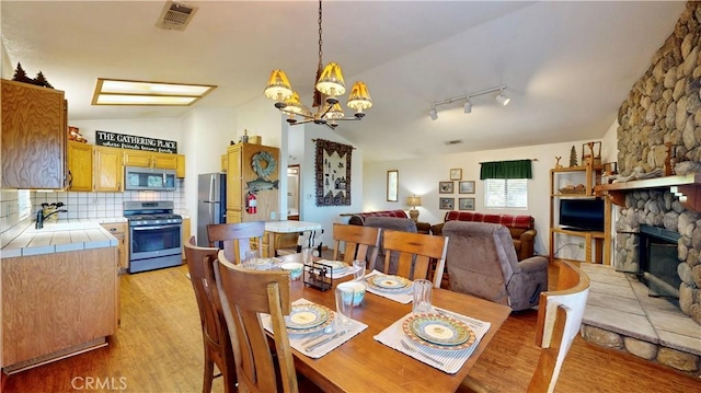 dining room featuring lofted ceiling, a stone fireplace, sink, light wood-type flooring, and a chandelier