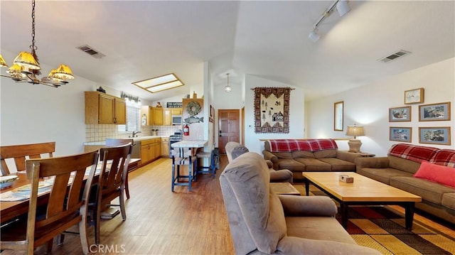 living room featuring vaulted ceiling, track lighting, light hardwood / wood-style flooring, and sink