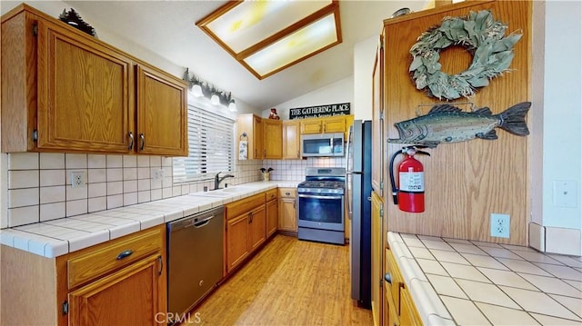 kitchen featuring sink, backsplash, tile countertops, appliances with stainless steel finishes, and light wood-type flooring