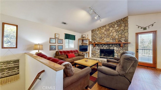 living room featuring a stone fireplace, hardwood / wood-style floors, and vaulted ceiling