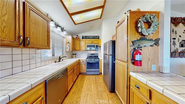 kitchen featuring appliances with stainless steel finishes, light wood-type flooring, backsplash, sink, and lofted ceiling