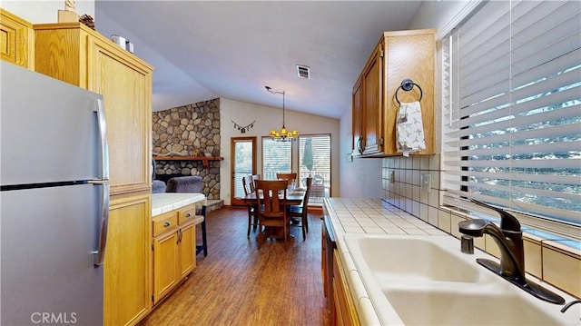 kitchen with tile countertops, dark hardwood / wood-style floors, stainless steel refrigerator, hanging light fixtures, and lofted ceiling