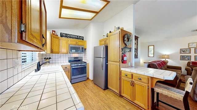 kitchen with sink, tile counters, a kitchen breakfast bar, decorative backsplash, and appliances with stainless steel finishes