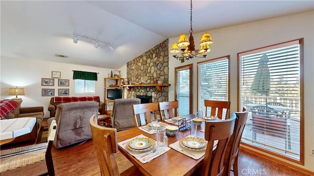 dining space featuring rail lighting, vaulted ceiling, hardwood / wood-style flooring, a fireplace, and a chandelier