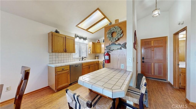 kitchen featuring sink, tile counters, hanging light fixtures, light hardwood / wood-style flooring, and stainless steel dishwasher