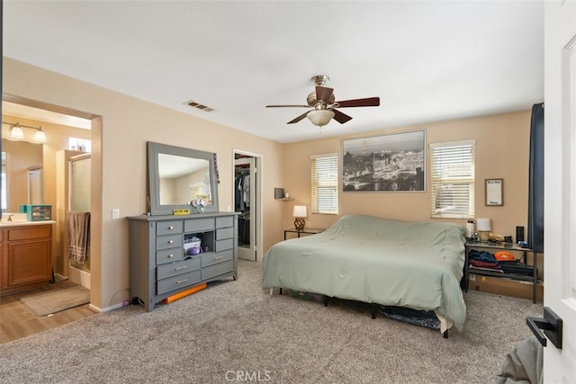 bedroom with a walk in closet, ceiling fan, light wood-type flooring, a closet, and ensuite bath