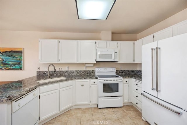 kitchen featuring dark stone counters, white appliances, sink, light tile patterned floors, and white cabinets