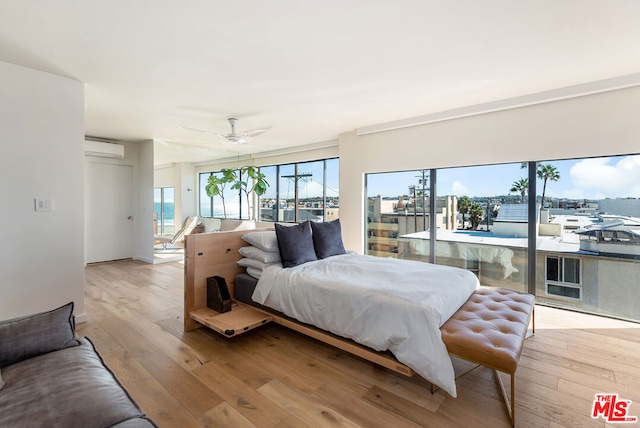 bedroom with ceiling fan, light wood-type flooring, and an AC wall unit