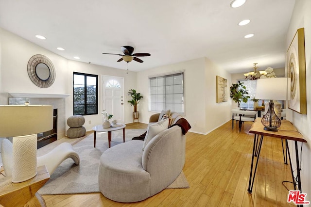 living room featuring ceiling fan with notable chandelier and light wood-type flooring