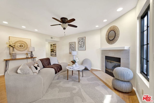 living room with ceiling fan, light wood-type flooring, and a tiled fireplace