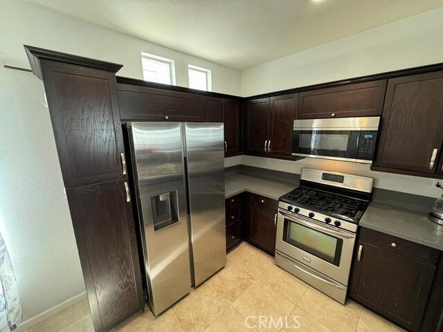 kitchen with dark brown cabinetry, light tile patterned floors, and appliances with stainless steel finishes