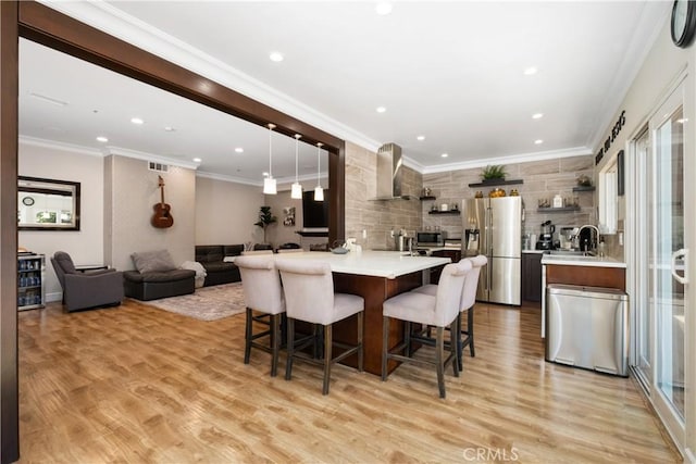 kitchen with pendant lighting, a breakfast bar area, light hardwood / wood-style floors, stainless steel refrigerator with ice dispenser, and wall chimney range hood