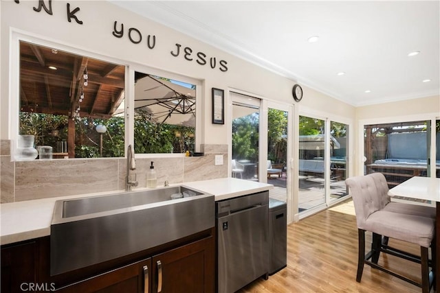 kitchen with sink, stainless steel dishwasher, ornamental molding, light hardwood / wood-style floors, and decorative backsplash