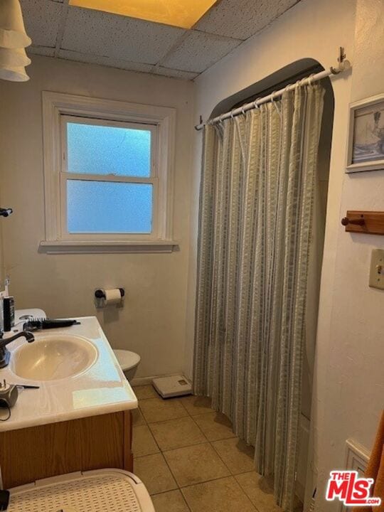 bathroom with toilet, a drop ceiling, vanity, and tile patterned flooring