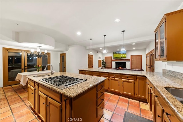 kitchen featuring pendant lighting, a center island with sink, sink, light stone countertops, and stainless steel gas cooktop