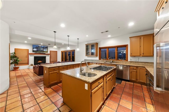 kitchen featuring appliances with stainless steel finishes, sink, decorative light fixtures, and an island with sink