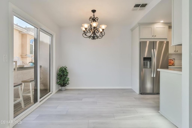 kitchen featuring hanging light fixtures, light hardwood / wood-style floors, white cabinets, stainless steel fridge with ice dispenser, and a chandelier