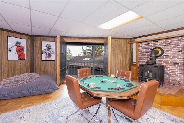 playroom with hardwood / wood-style flooring, a wood stove, a drop ceiling, and wooden walls