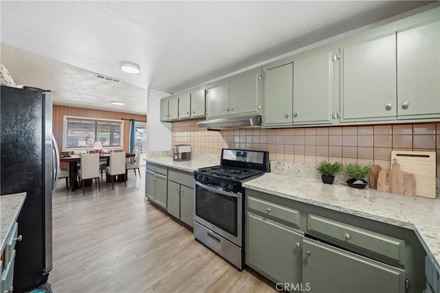 kitchen featuring backsplash, green cabinetry, light wood-type flooring, appliances with stainless steel finishes, and light stone counters