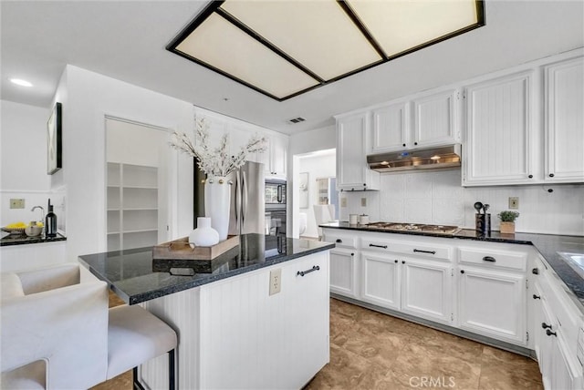 kitchen featuring white cabinets, a kitchen breakfast bar, decorative backsplash, dark stone countertops, and appliances with stainless steel finishes