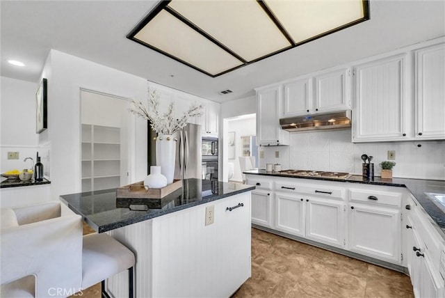 kitchen with white cabinetry, stainless steel appliances, dark stone counters, decorative backsplash, and a breakfast bar