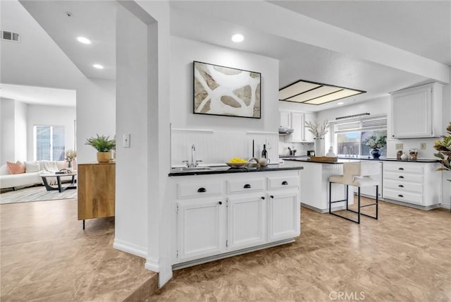 kitchen featuring plenty of natural light, a kitchen bar, white cabinetry, and sink