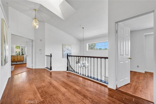 hallway featuring high vaulted ceiling, wood-type flooring, and a notable chandelier