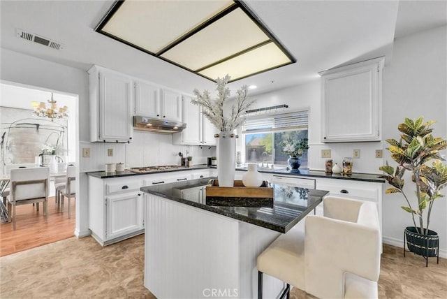 kitchen with a center island, an inviting chandelier, white cabinets, dark stone countertops, and stainless steel gas cooktop