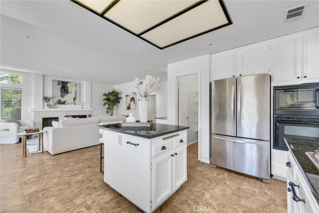 kitchen with a center island, a brick fireplace, stainless steel fridge, white cabinetry, and black microwave