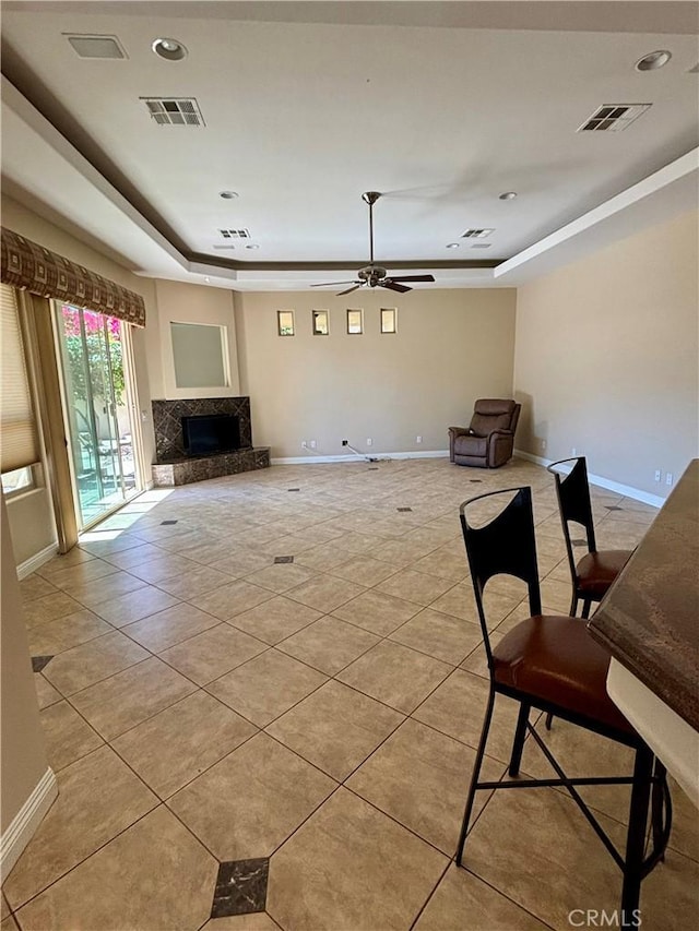 unfurnished living room with ceiling fan, light tile patterned floors, a high end fireplace, and a raised ceiling