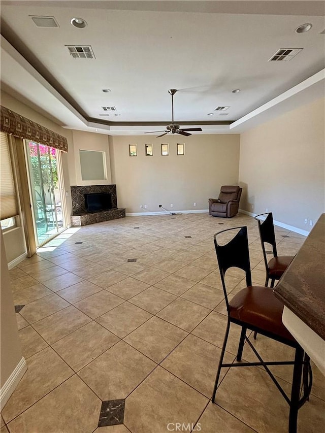 unfurnished living room featuring ceiling fan, a premium fireplace, a tray ceiling, and light tile patterned floors