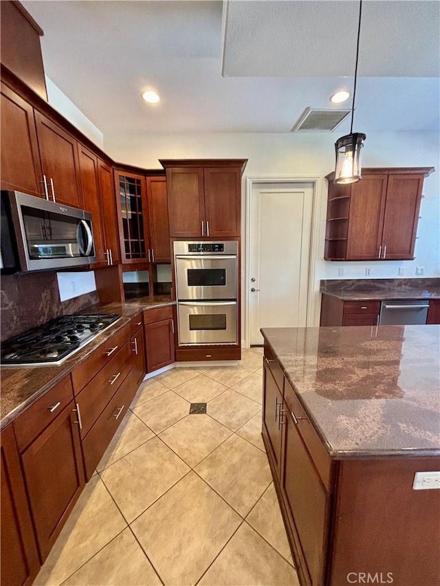 kitchen featuring pendant lighting, stainless steel appliances, light tile patterned floors, and dark stone countertops