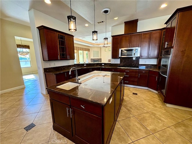 kitchen featuring sink, hanging light fixtures, appliances with stainless steel finishes, a wealth of natural light, and a kitchen island with sink