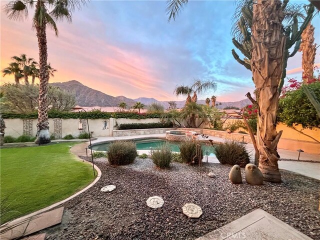 pool at dusk featuring an in ground hot tub, a mountain view, and a lawn