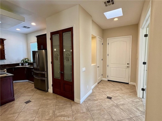 kitchen featuring sink, stainless steel fridge with ice dispenser, light tile patterned floors, a skylight, and dark brown cabinetry