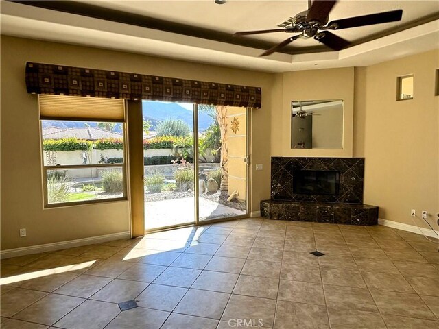 entryway with ceiling fan, tile patterned flooring, a fireplace, and a tray ceiling