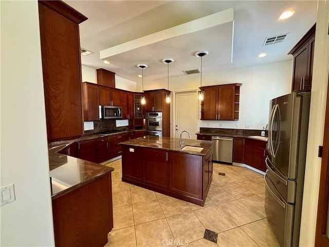 kitchen with light tile patterned flooring, appliances with stainless steel finishes, pendant lighting, sink, and a kitchen island with sink